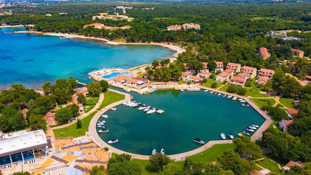 Vista aérea de un complejo turístico costero con un puerto deportivo, piscina y edificios residenciales.
