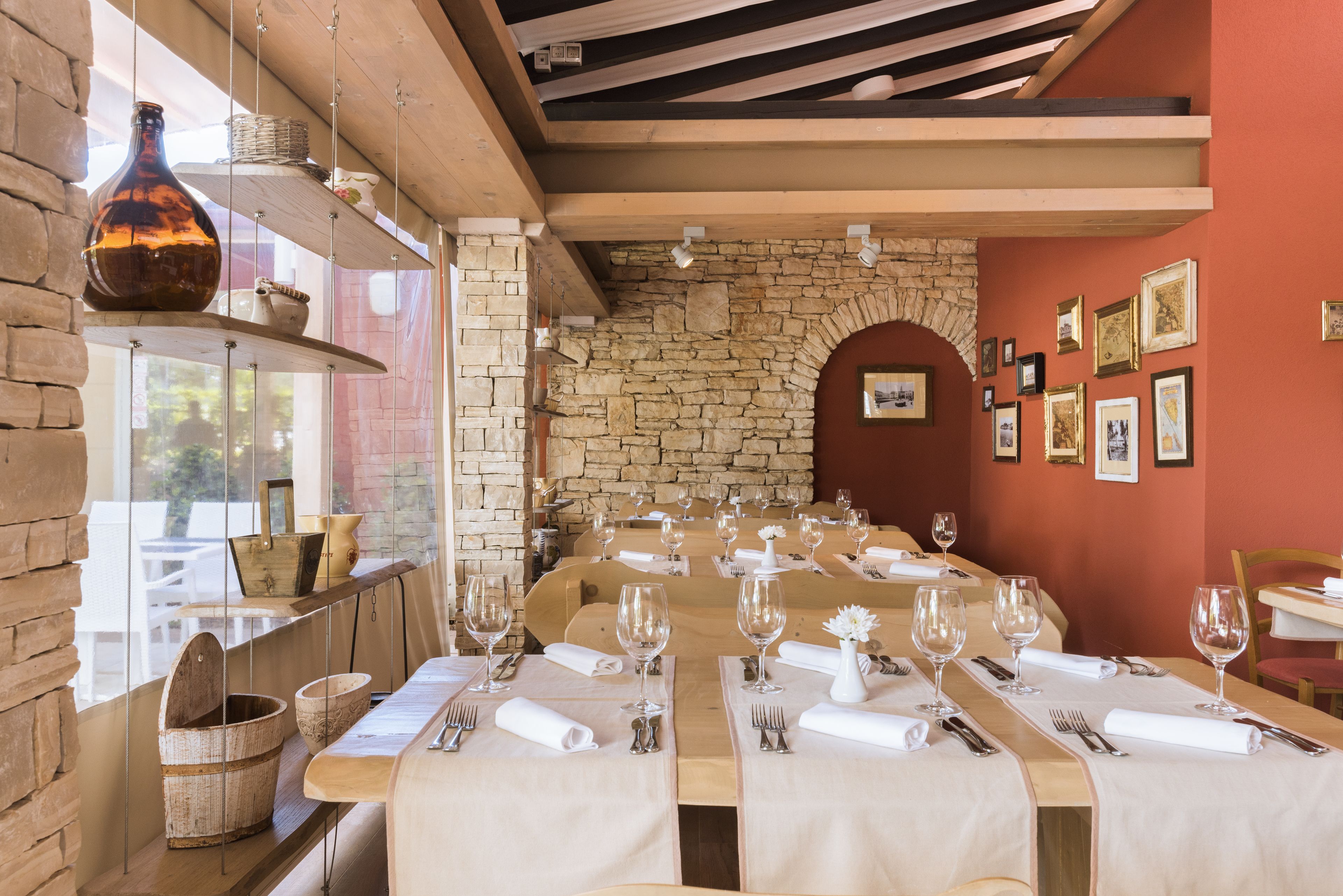 A restaurant with a long wooden table set for dining, stone walls, and framed pictures on the wall.