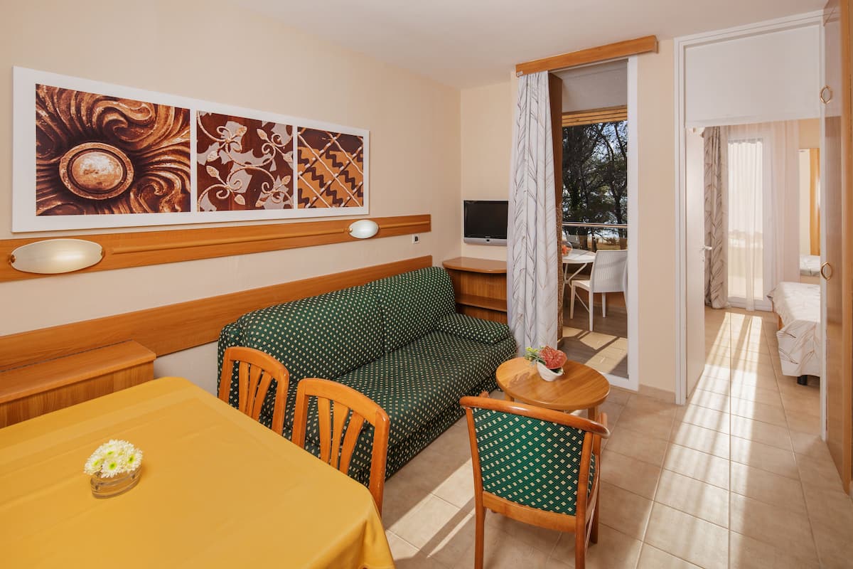 Hotellihuone, jossa on sohva, ruokapöytä, tuoleja, televisio ja taideteoksia seinällä.