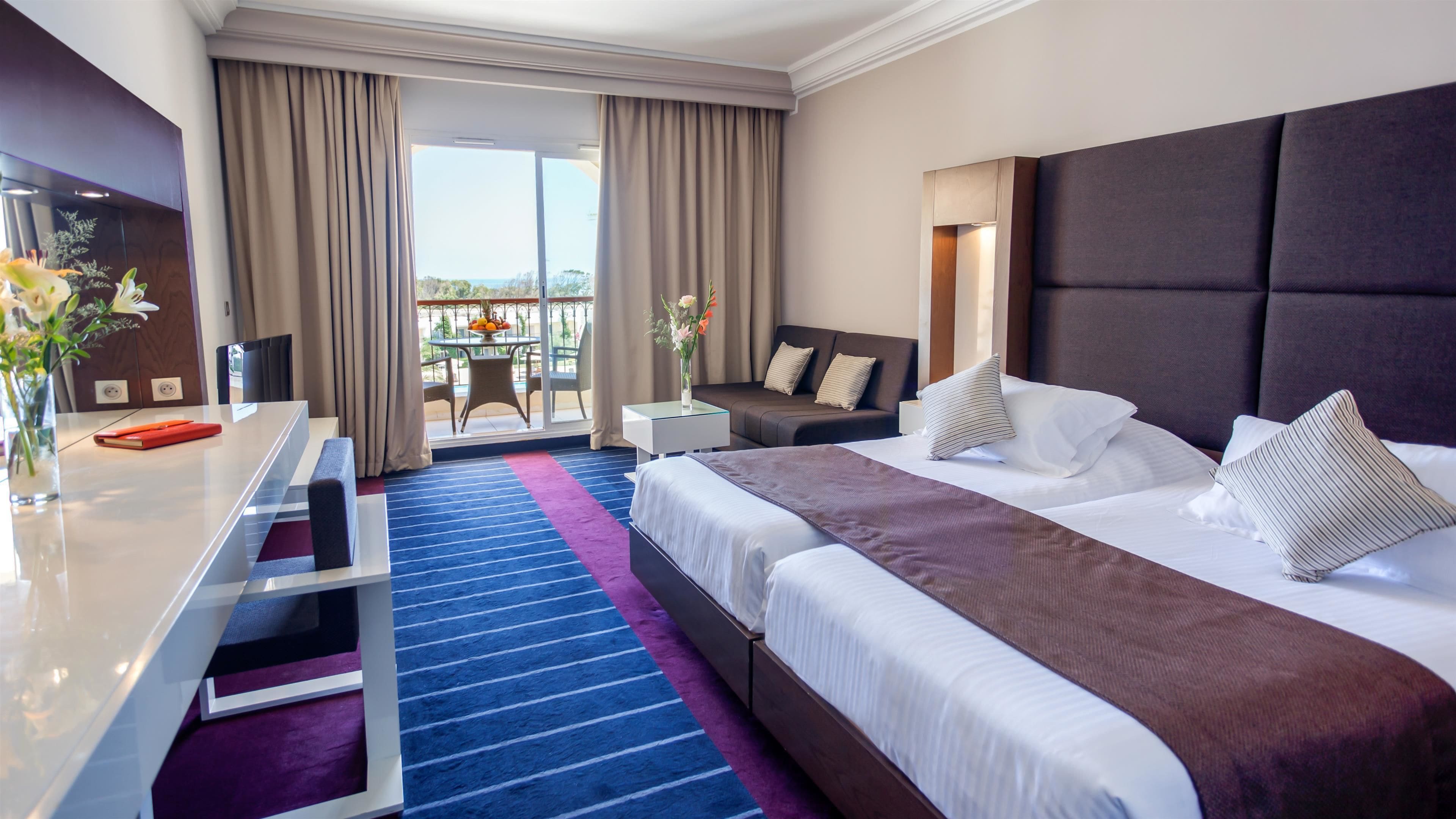 A hotel room with a large bed, a desk, and a balcony with a table and chairs.