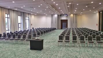 A conference room with rows of chairs, a central table, and large windows with curtains.