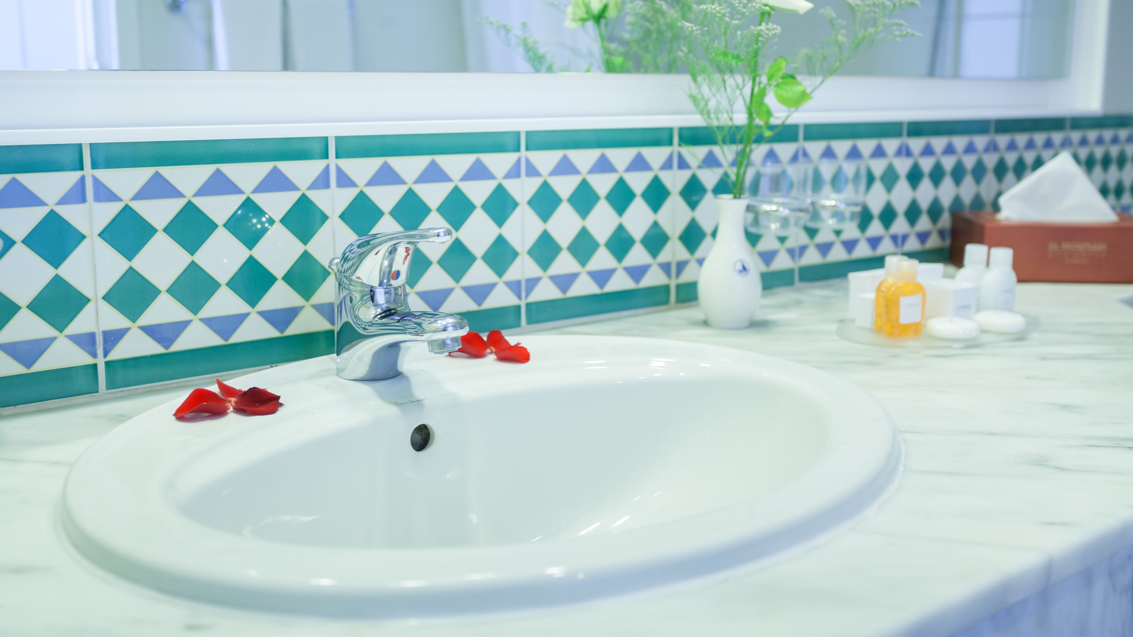 Ein Badezimmerwaschbecken mit einem modernen Wasserhahn, einer dekorativen Fliesenrückwand und Pflegeprodukten auf der Ablagefläche.