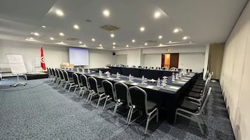 Une salle de conférence avec une longue table, des chaises, un écran de projection et un drapeau rouge.