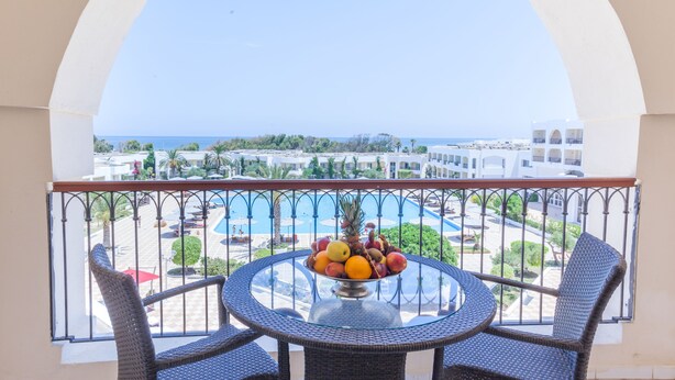 A balcony with wicker chairs and a glass table, overlooking a swimming pool and a coastal view. - El Mouradi Gammarth (La Marsa)