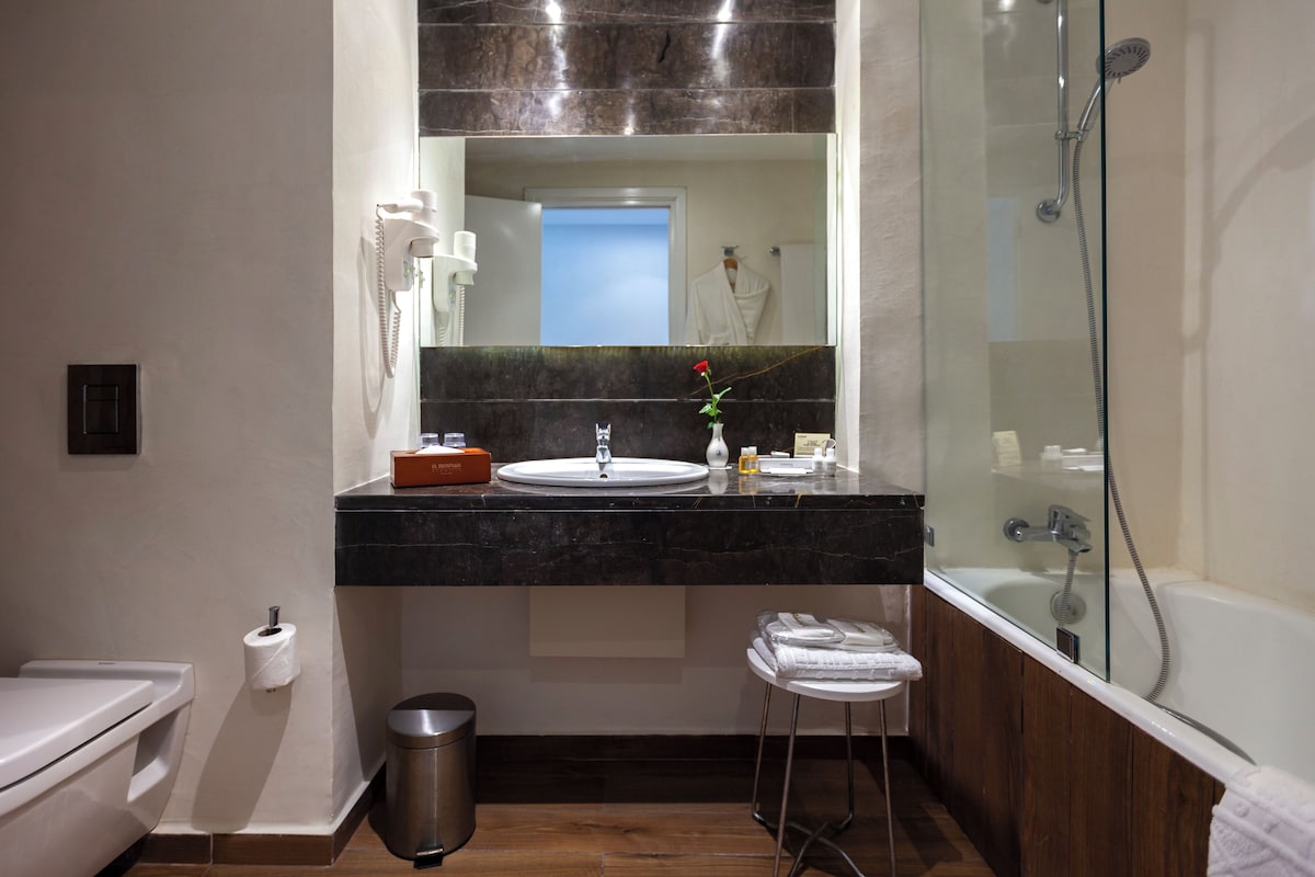A modern bathroom with a marble countertop, a sink, a mirror, a toilet, a trash can, and a shower.