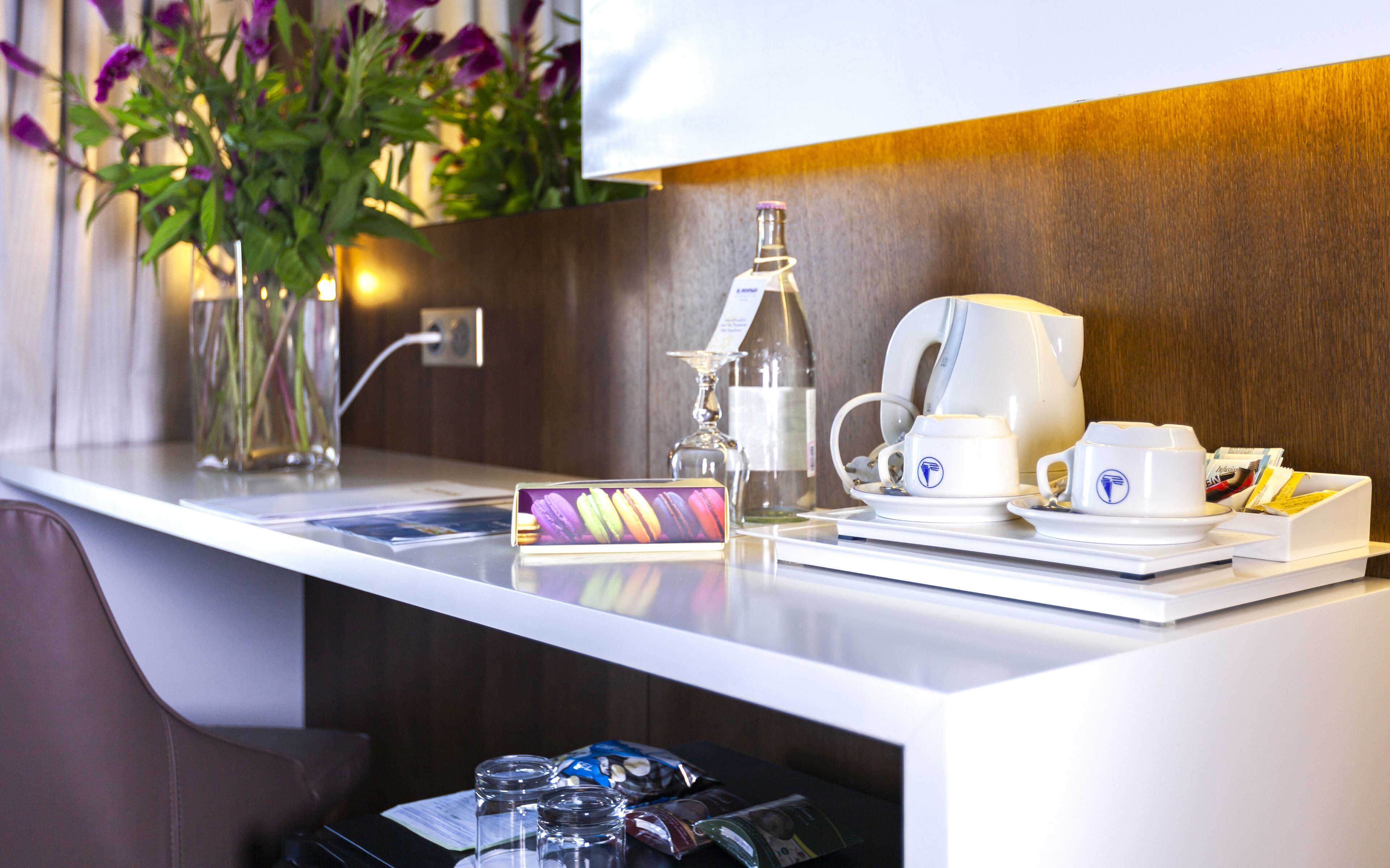 A hotel reception area with a coffee station, a wine bottle, a vase with flowers, and a menu.