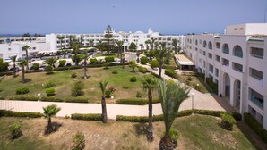Een resort met meerdere witte gebouwen, een centrale binnenplaats met palmbomen en uitzicht op zee.