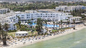 Een resort met een groot zwembad, meerdere gebouwen en een strand met ligbedden.