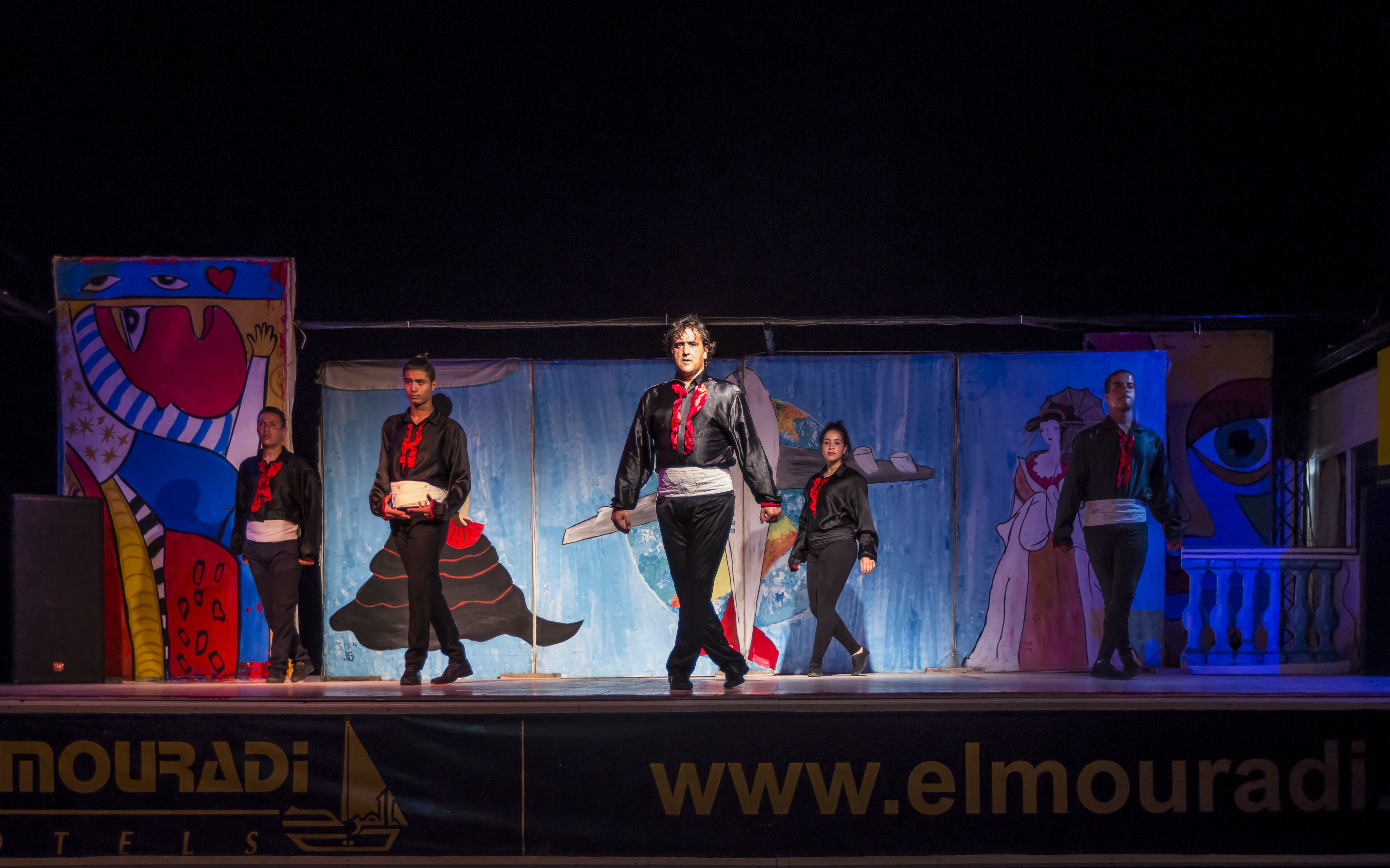 A stage with performers in costumes, a banner with hotel name, and a website address.