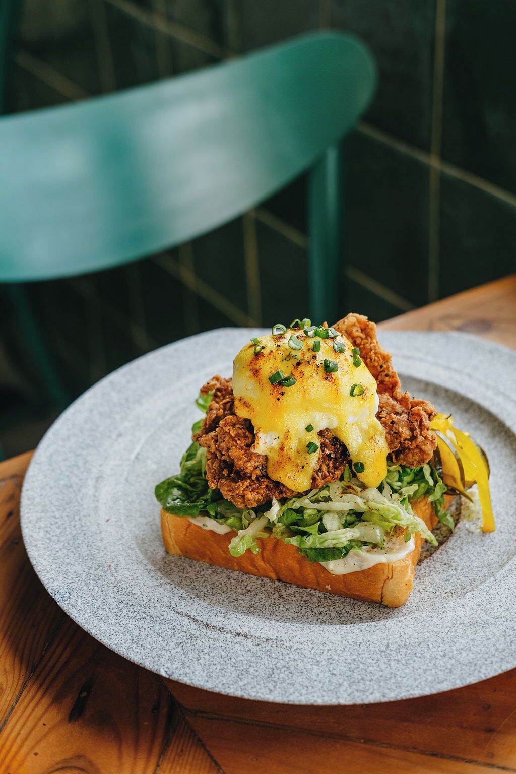 A sandwich with fried chicken, greens, and a fried egg on a round plate.