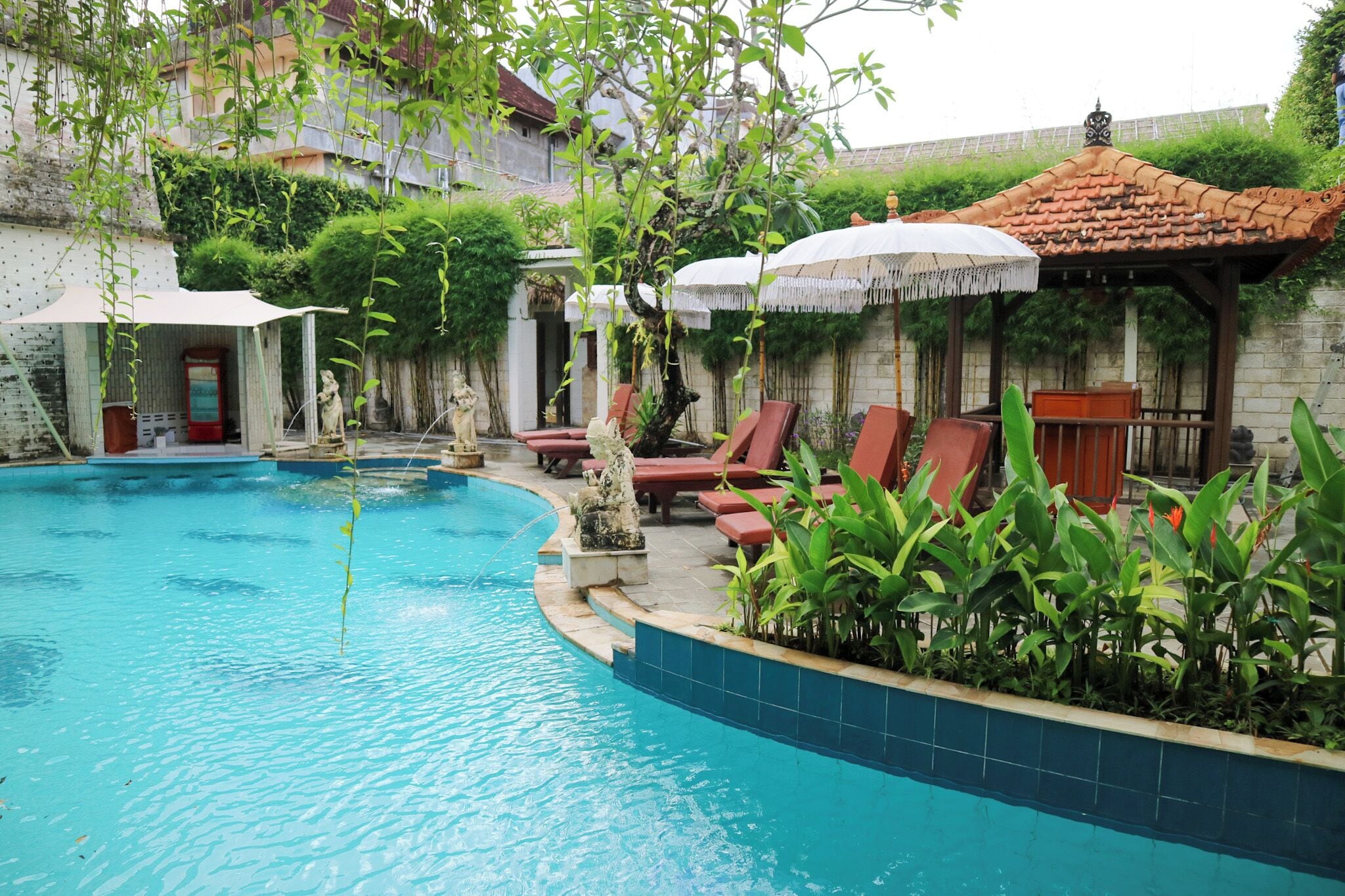 A swimming pool with red lounge chairs and umbrellas, surrounded by greenery and stone walls.