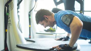 Una persona usando una bicicleta estática en un gimnasio, con una cinta de correr al fondo.