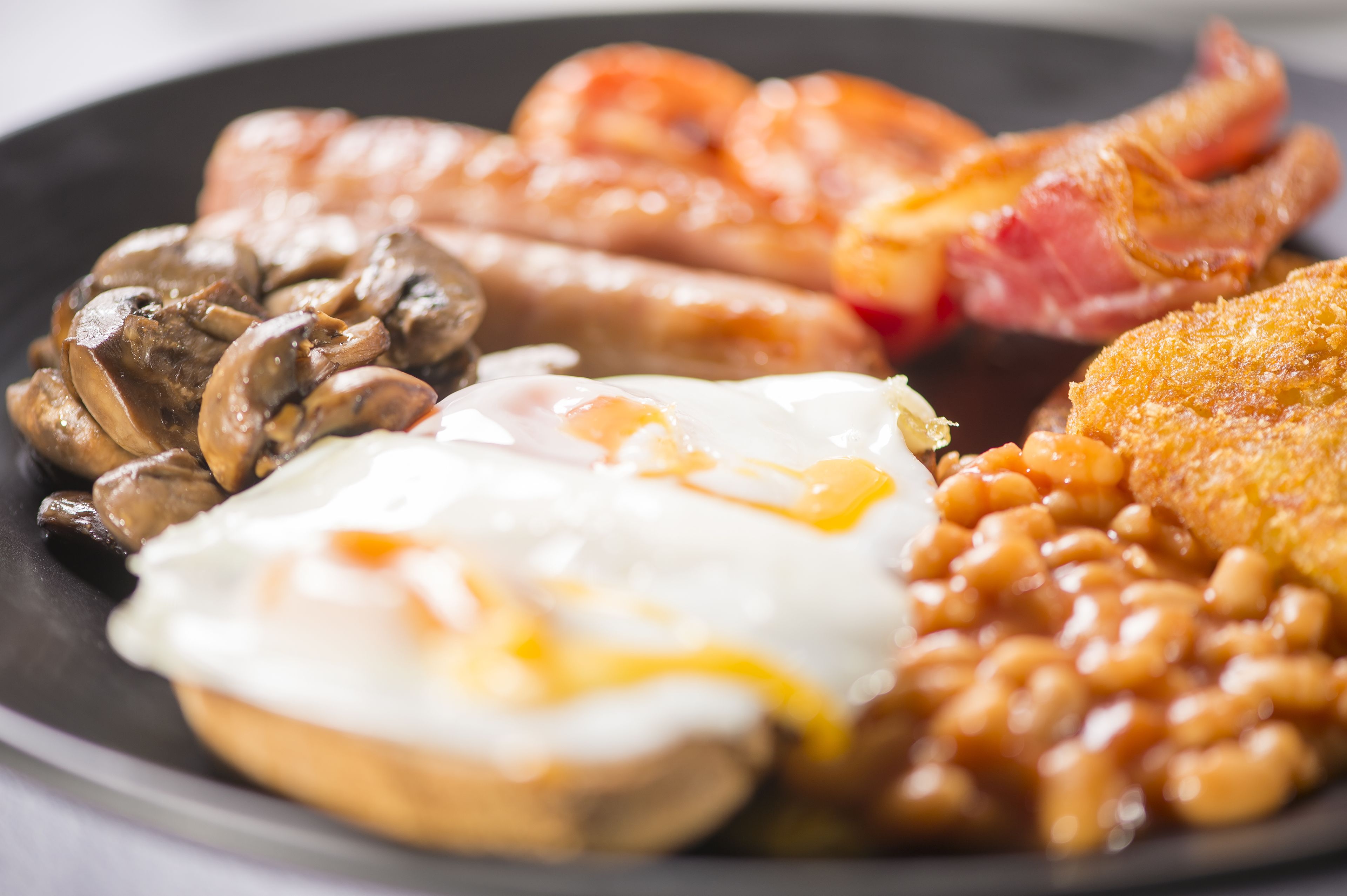 Une assiette de nourriture pour le petit-d éjeuner comprenant des œufs, des saucisses, du bacon, des champignons, des haricots cuits et un aliment frit.