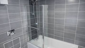 Un bany modern amb dutxa tancada per vidre, una banyera blanca i una petita planta en test.