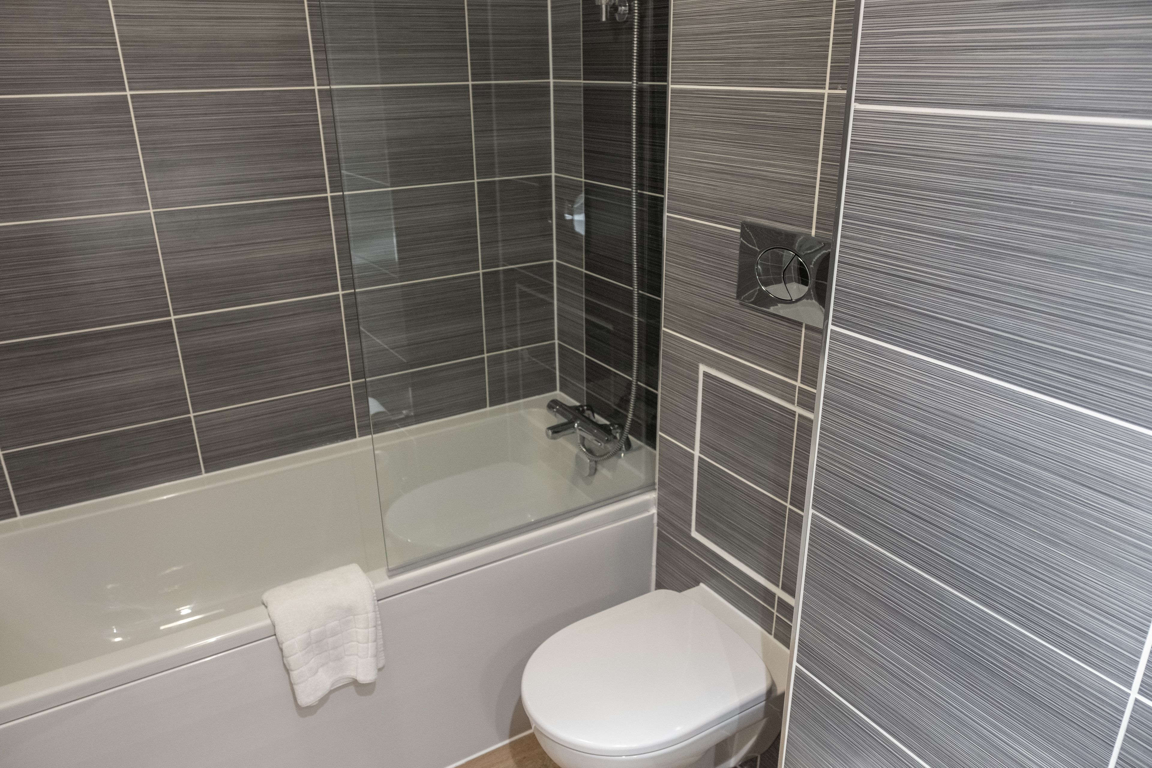 A modern bathroom with a bathtub, toilet, and glass shower enclosure.