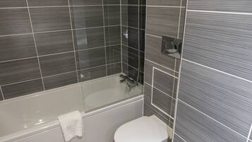 A modern bathroom with a bathtub, toilet, and glass shower enclosure.