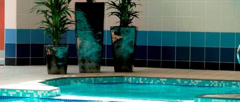 Una piscina con bordes de azulejos y tres grandes macetas con plantas al fondo.