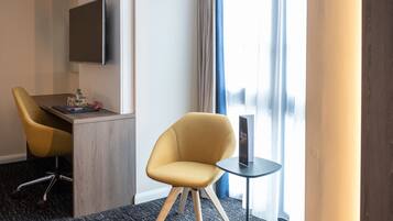 Ett hotellrum med modern design, inrett med en gul fåtölj, ett litet bord, en platt-TV som är monterad på väggen och en utsikt över omgivningarna genom stora fönster.