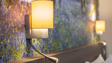 A wall-mounted lamp with a modern design, positioned above a wooden headboard in a room with a textured floral wall.