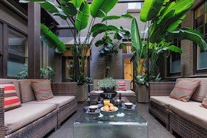 A cozy outdoor seating area with wicker sofas, a glass coffee table, and a variety of plants. - Vulcan Hotel Sydney (Ultimo)