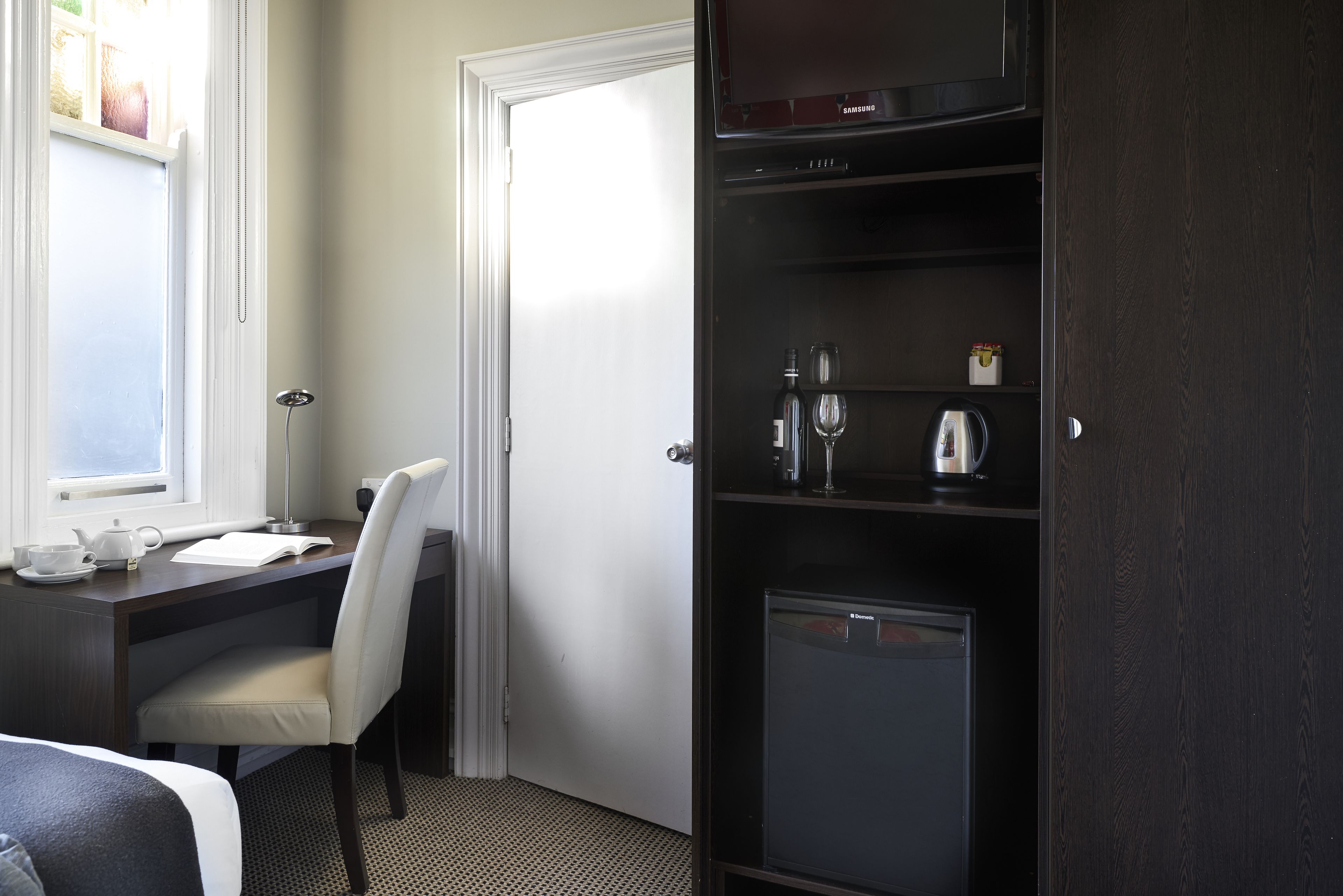 A hotel room with a desk, chair, and a minibar.
