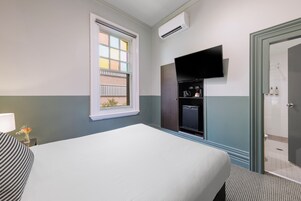 Una camera d'albergo con un letto, una TV a muro, una finestra con vista e un ingresso che conduce al bagno.