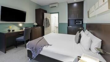 Une chambre d’hôtel avec un grand lit, un bureau avec une chaise, une télévision, un four à micro-ondes et une salle de bain visible à travers une porte ouverte.
