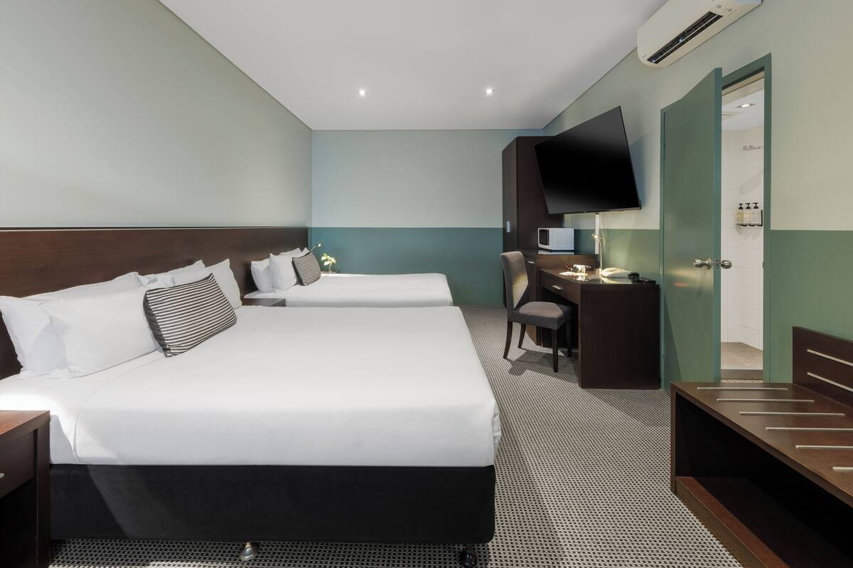 A hotel room with two beds, a desk, a chair, a TV, and an air conditioning unit.