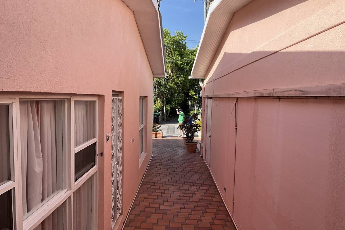 A narrow brick pathway between buildings with pink walls and white window frames.
