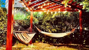 A hammock under a wooden pergola with string lights, surrounded by lush greenery and a building in the background. - The Monteray Hotel (St. Lawrence Gap)