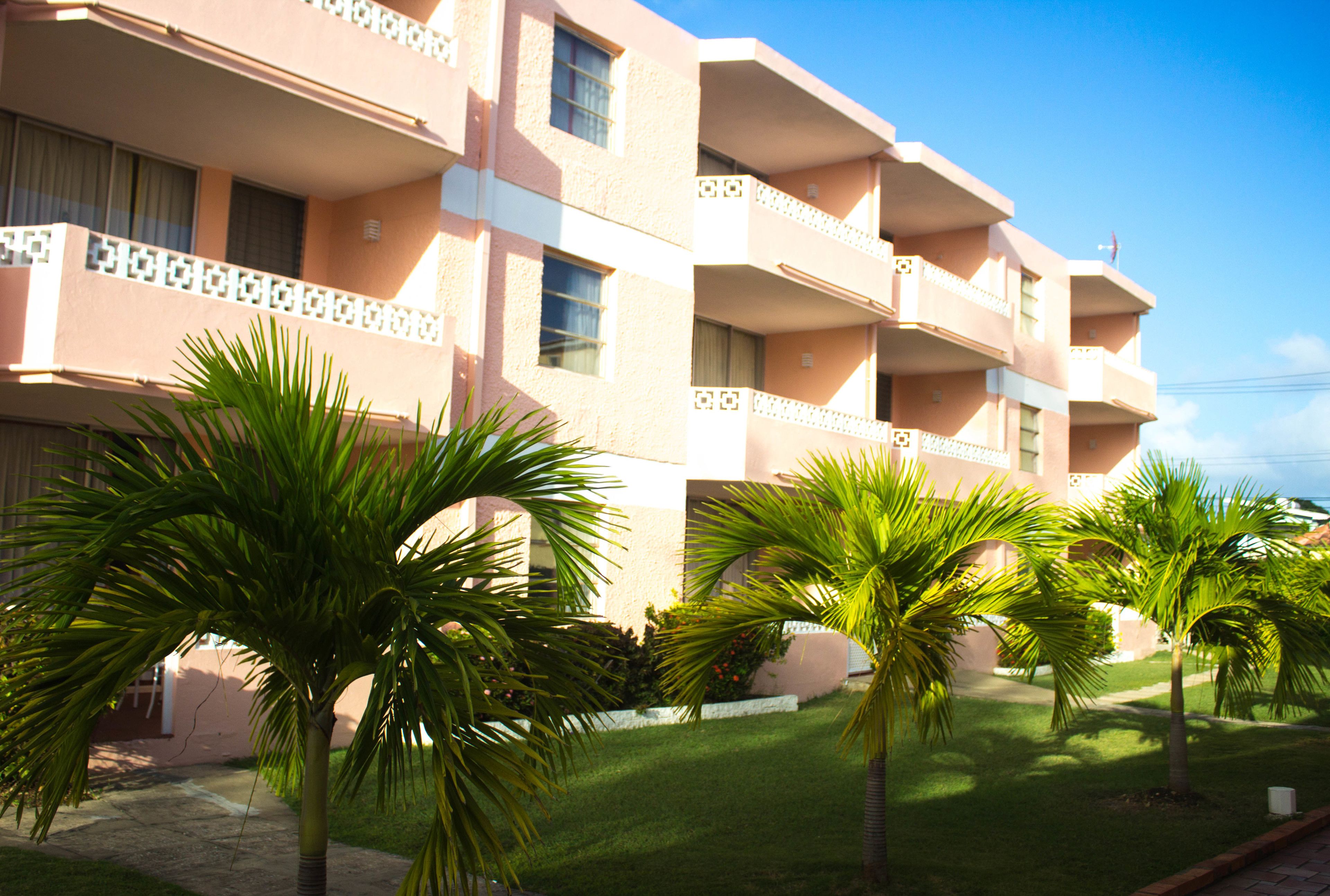 A multi-story hotel with balconies and a well-maintained lawn with palm trees.