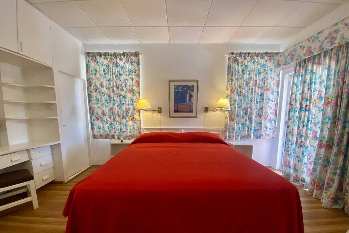 A room with a bed, two bedside tables with lamps, a wardrobe, and floral curtains.