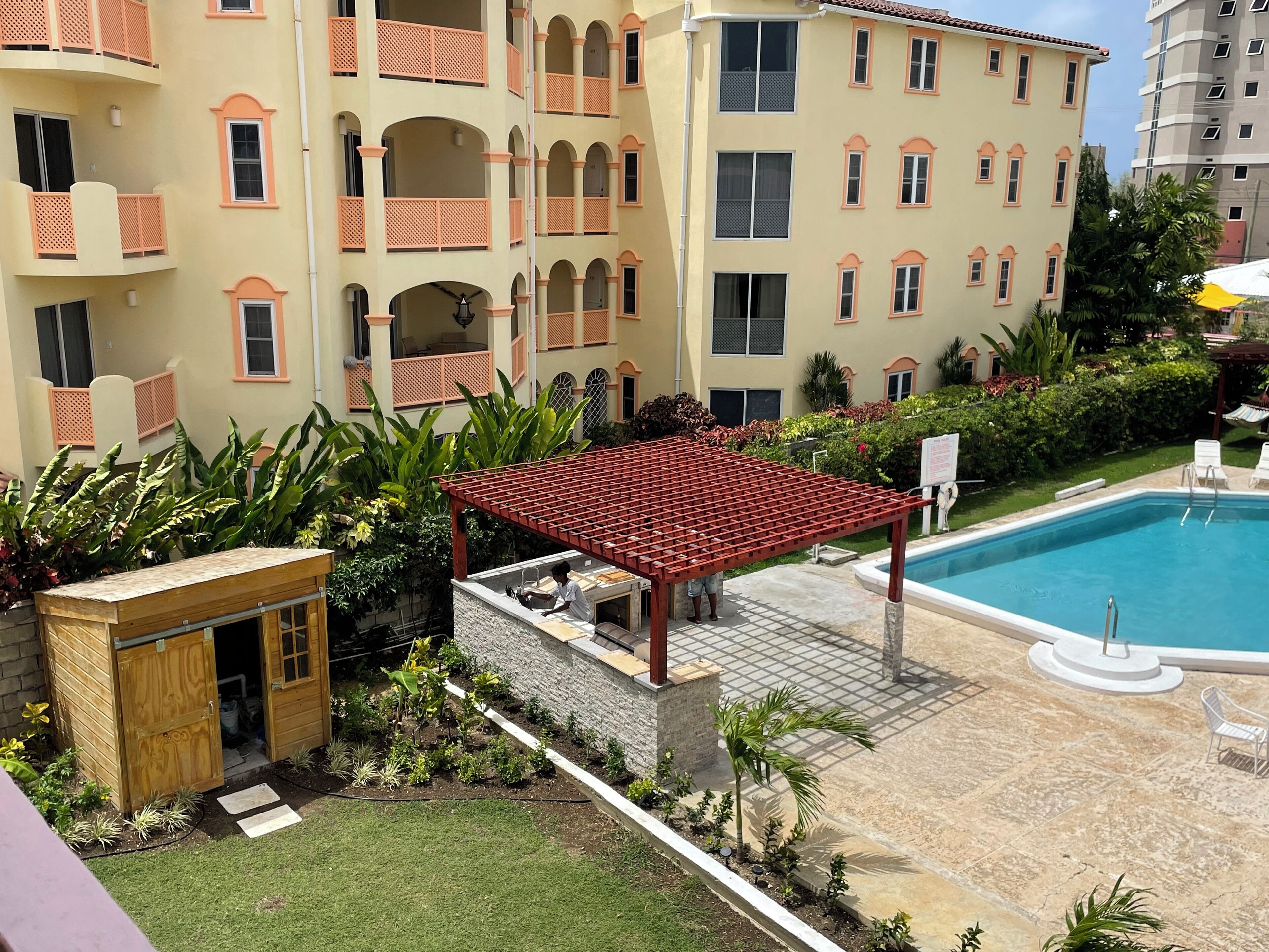 Ein Poolbereich mit Pergola, einer kleinen Holzkonstruktion und einem gepflegten Garten.