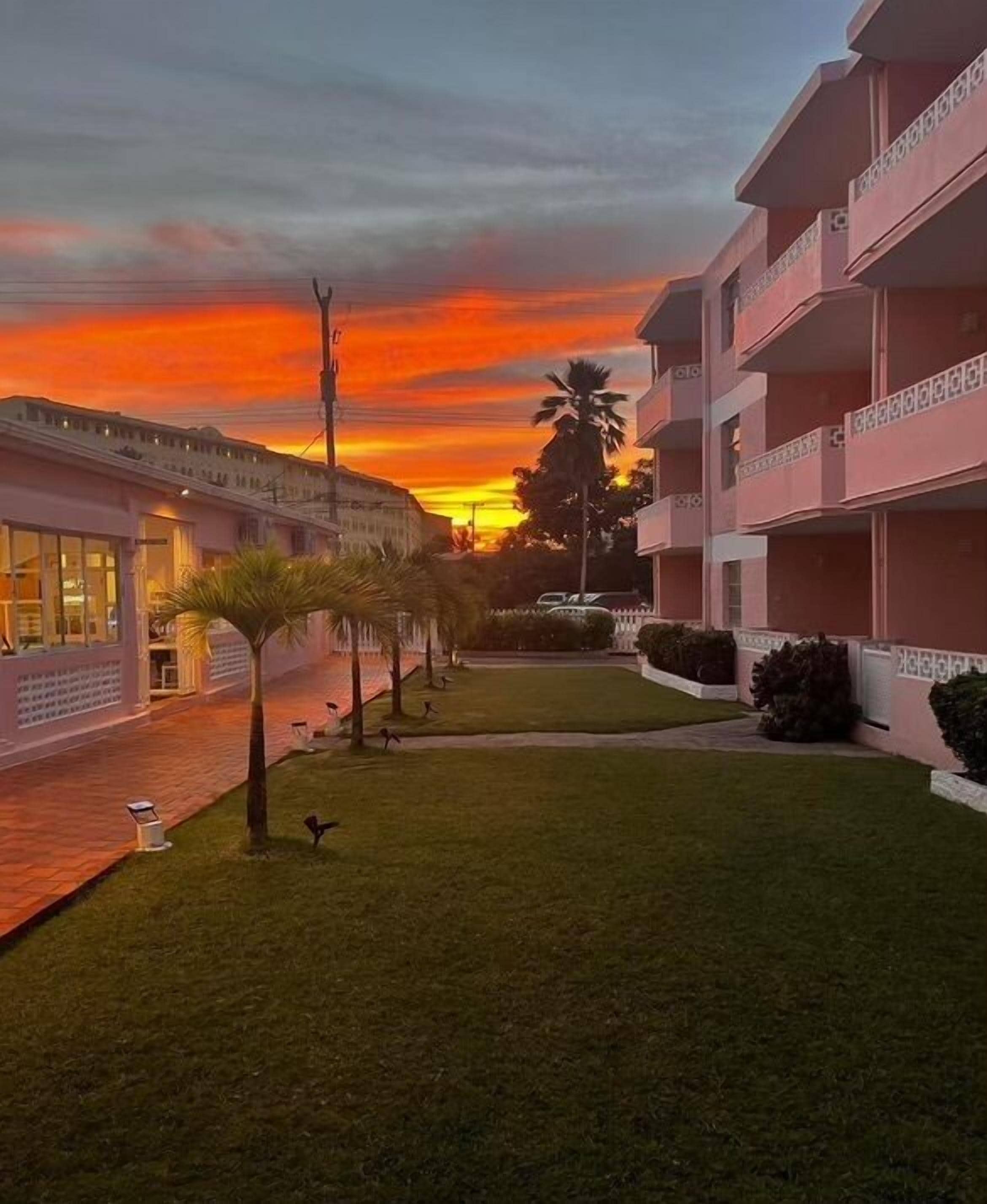 A hotel courtyard with a sunset view, palm trees, and a building with balconies.