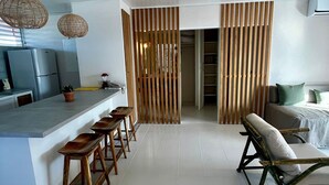 A modern kitchen with a bar area, wooden slatted partition, and a seating area with a sofa and chairs. - The Monteray Hotel (St. Lawrence Gap)