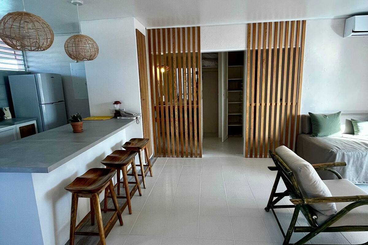 A modern kitchen with a bar area, wooden slatted partition, and a seating area with a sofa and chairs.