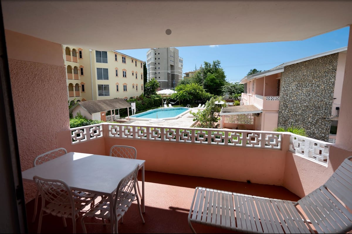 A balcony with a pool, white chairs, and a table.