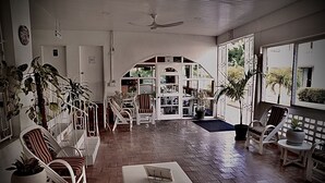A spacious indoor area with a brick floor, white furniture, and large windows offering views of the outdoors. - The Monteray Hotel (St. Lawrence Gap)
