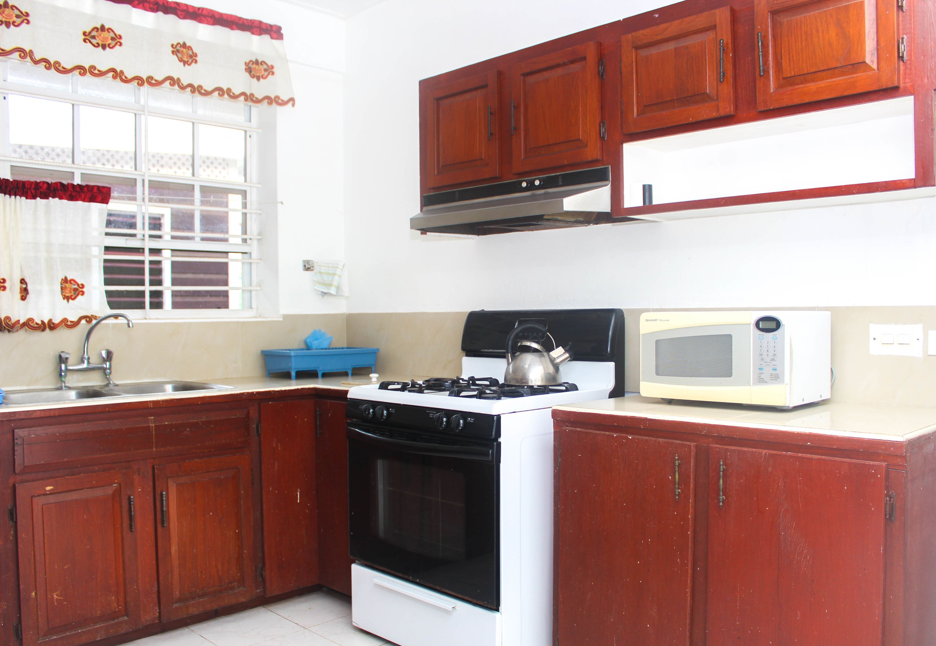 A kitchen with wooden cabinets, a stove, a kettle, and a microwave.