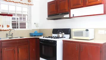 A kitchen with wooden cabinets, a stove, a kettle, and a microwave.