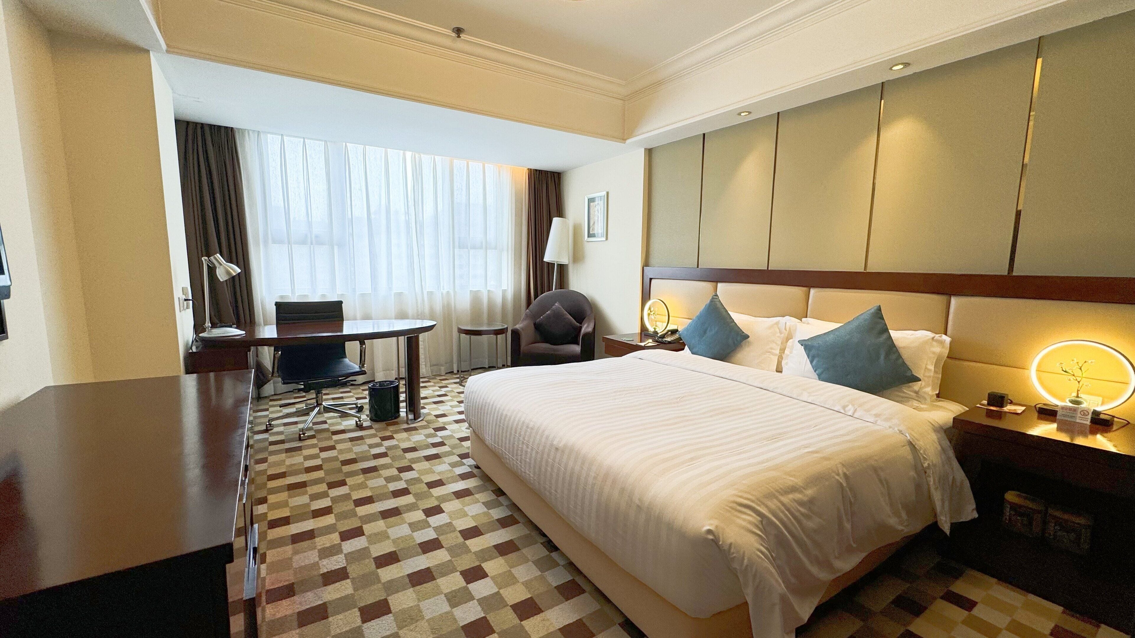 A hotel room with a large bed, a desk, a chair, and a small table.