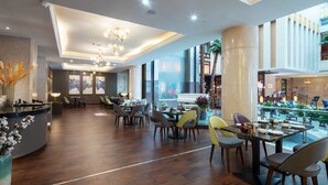 Een ruime lobby met een hoge plafond, moderne kroonluchters en een centraal gelegen zithoek met tafels en stoelen.