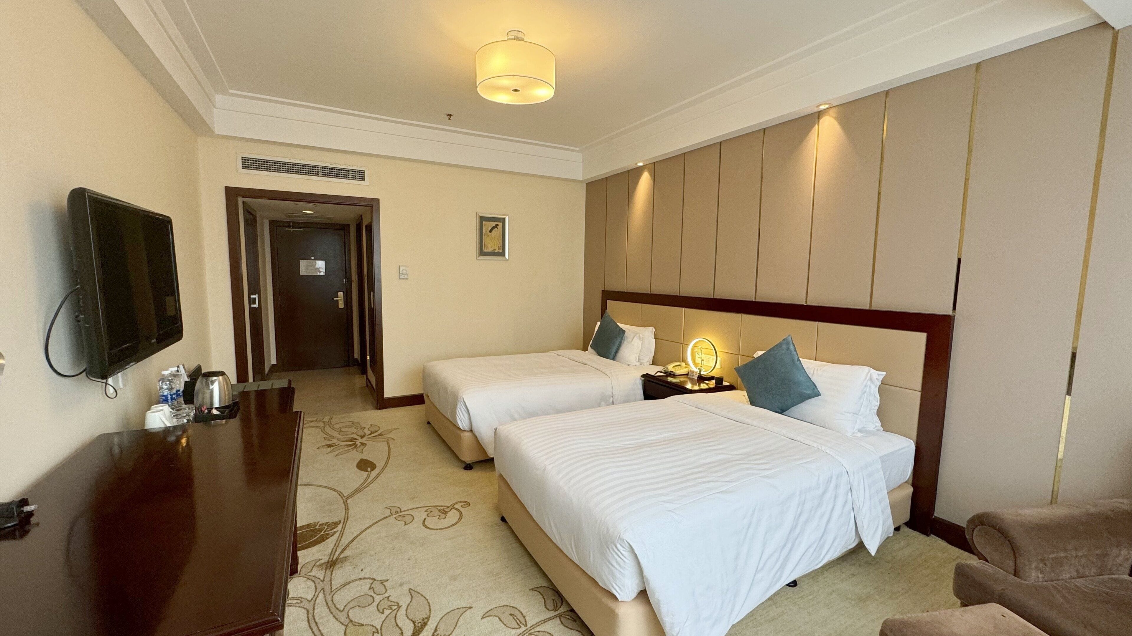 A hotel room with two beds, a desk, a television, and a mirror.