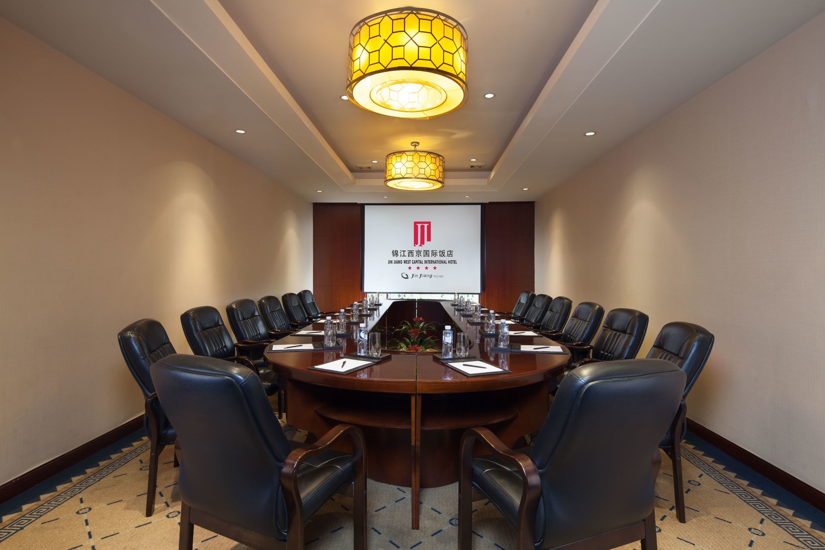 Une salle de conférence équipée d’une grande table, de nombreuses chaises et d’un écran de projection affichant un logo.