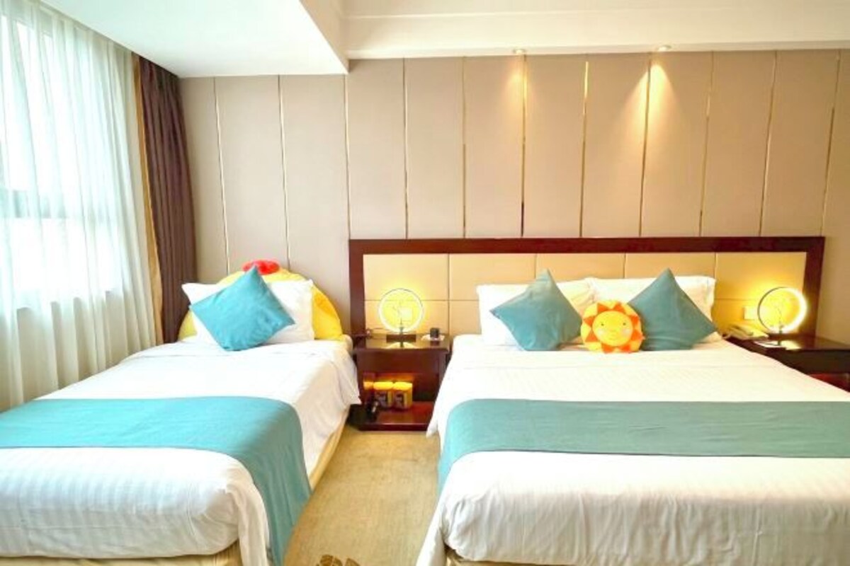 A hotel room with two beds, each with a headboard, bedside tables, and lamps.