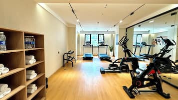 Un gimnasio con equipo de ejercicio, estantes para botellas de agua y un espejo que refleja el espacio.