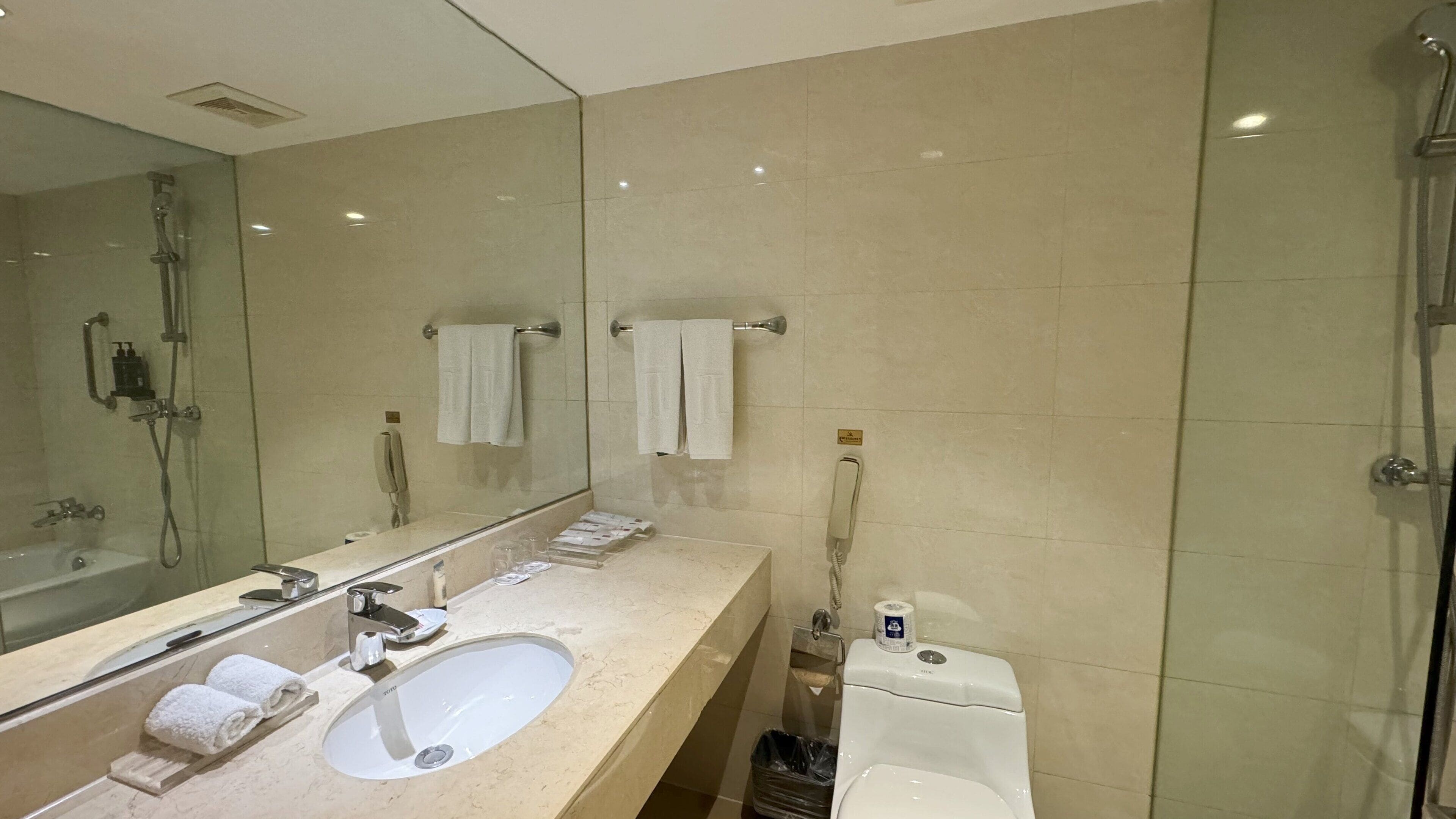 A modern bathroom with a large mirror, a sink, a toilet, and a shower.