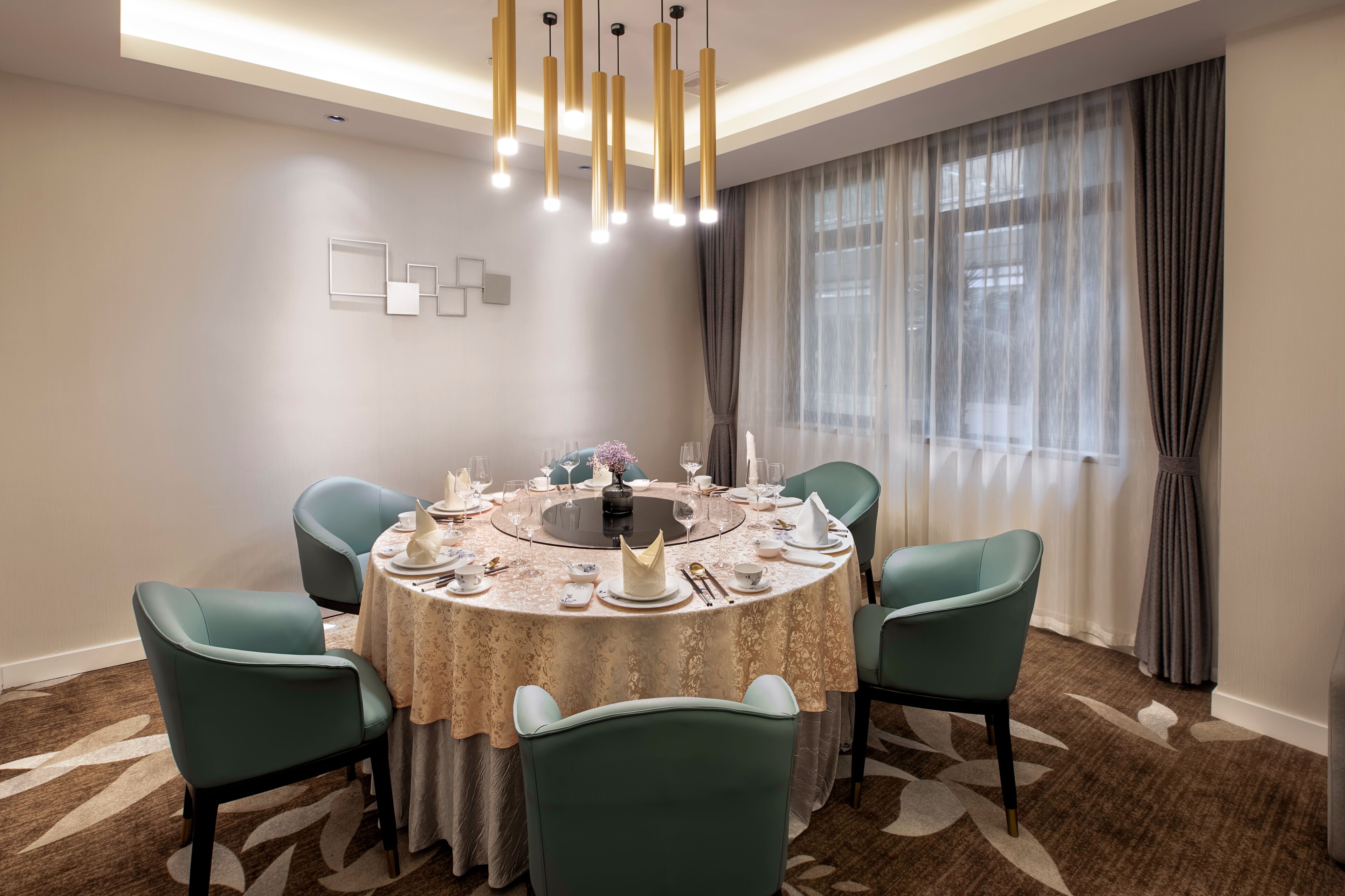 A dining area with a round table set for six, surrounded by teal chairs, under a modern chandelier.