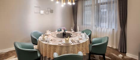 A dining area with a round table set for six, surrounded by teal chairs, under a modern chandelier.