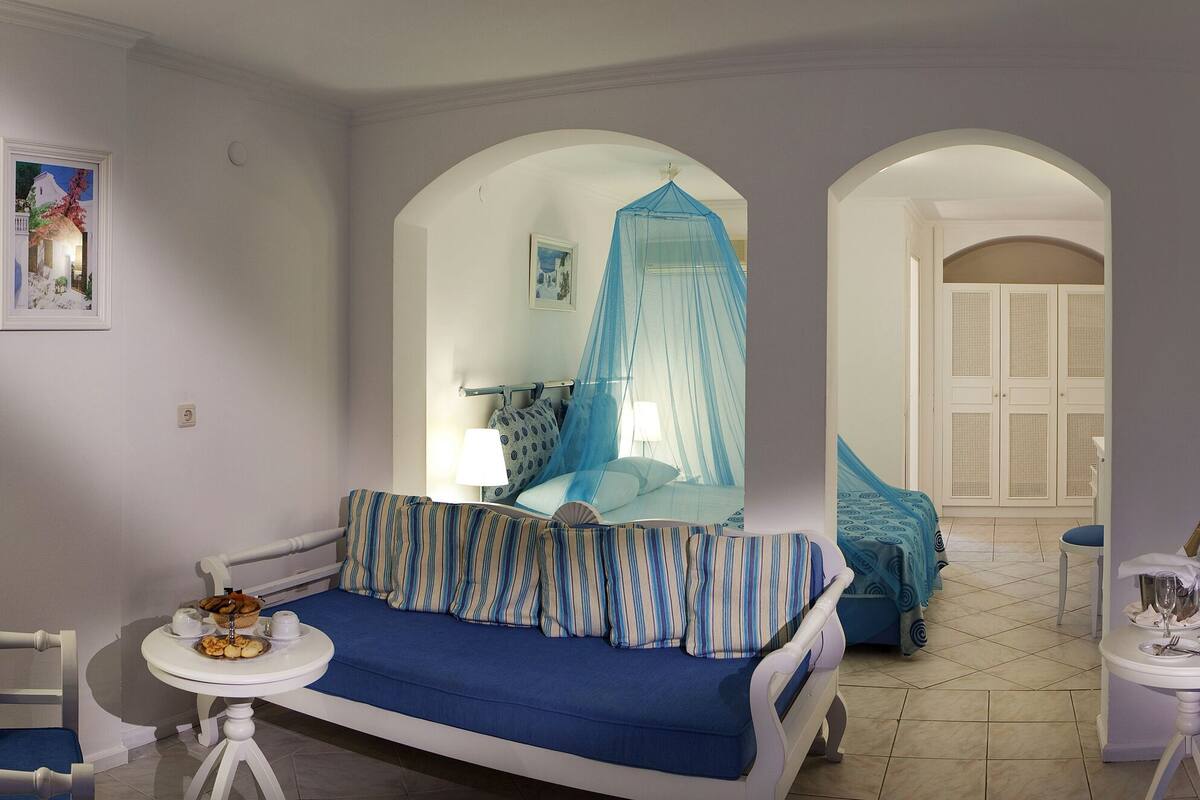 A room with a blue sofa, a striped sofa, a small table with a tray of food, and a bed with a canopy.